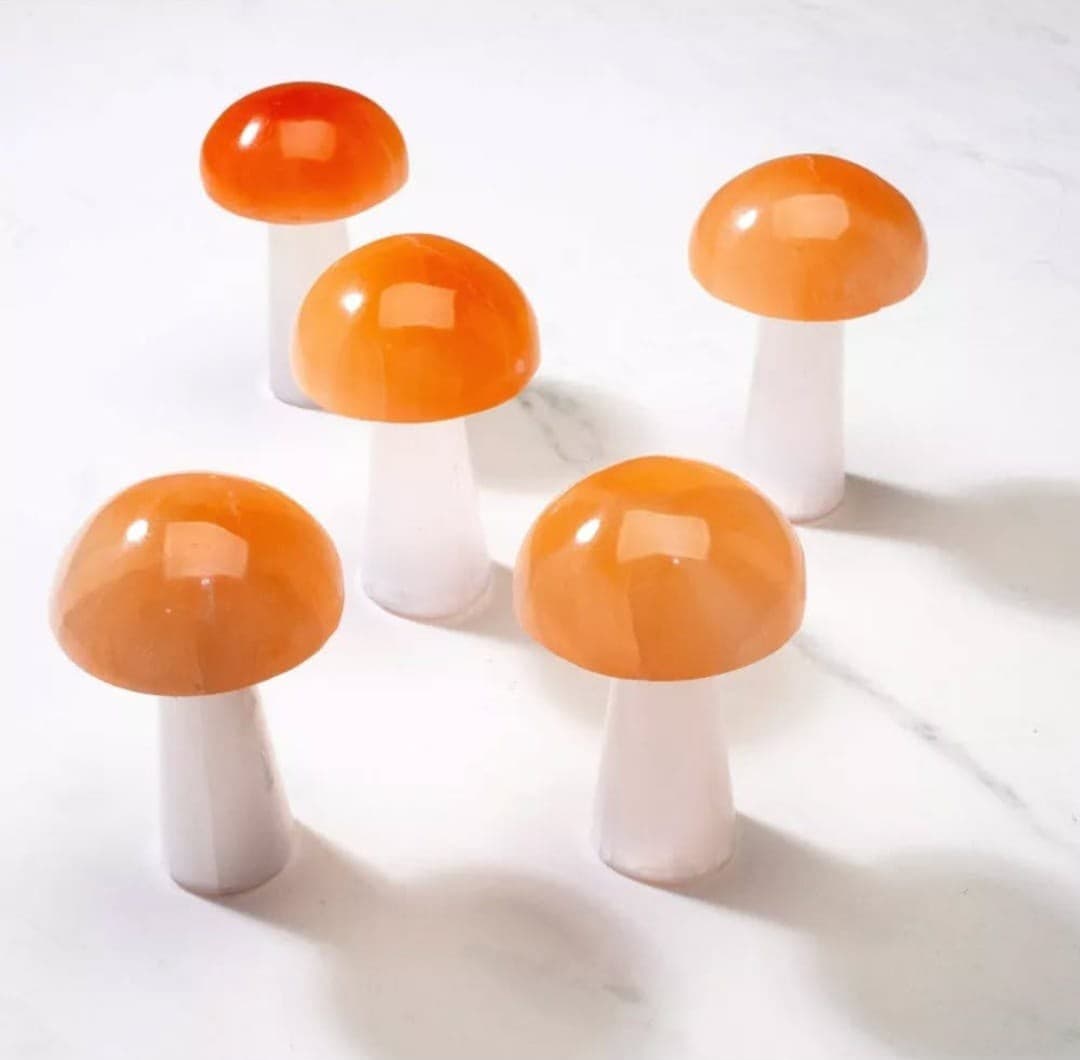 Five small crystal mushrooms with bright orange caps and white stems on a marble surface.