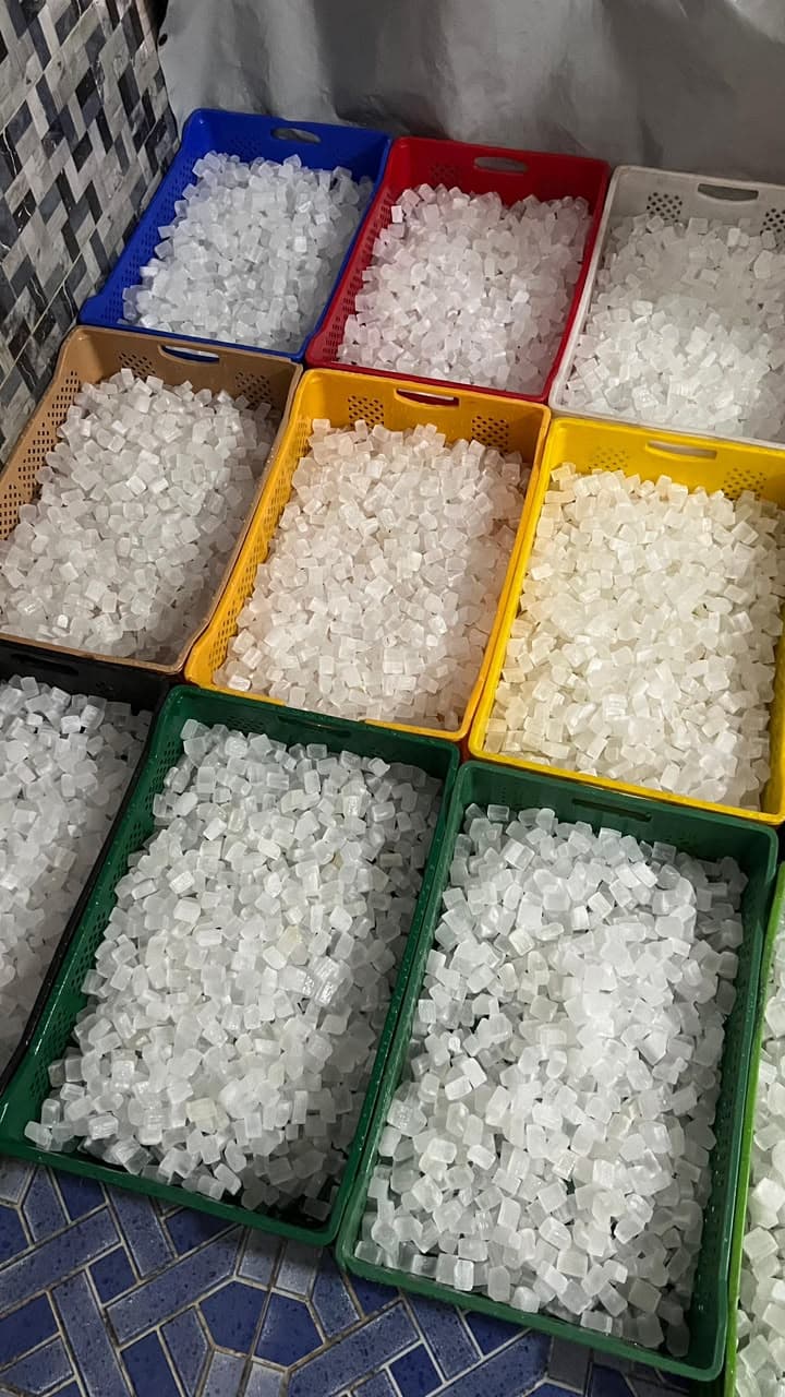 Colorful plastic crates filled with translucent white crystalline cubes on a blue tiled floor.