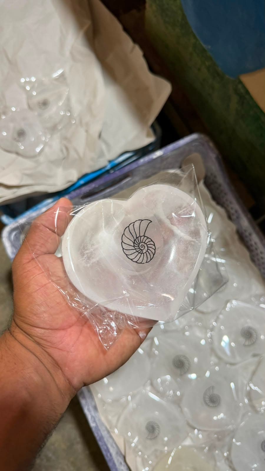 Hand holding a heart-shaped white selenite bowl with a black nautilus shell design.