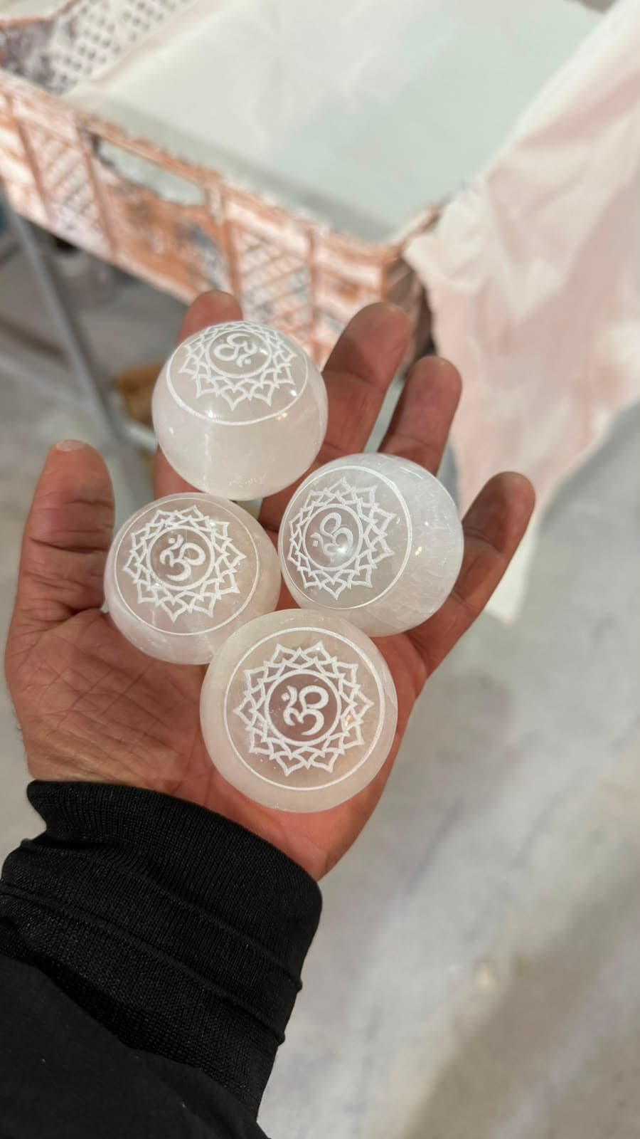 Mano sosteniendo cuatro esferas de selenita blanca con símbolos Om grabados dentro de mandalas de loto decorativos.