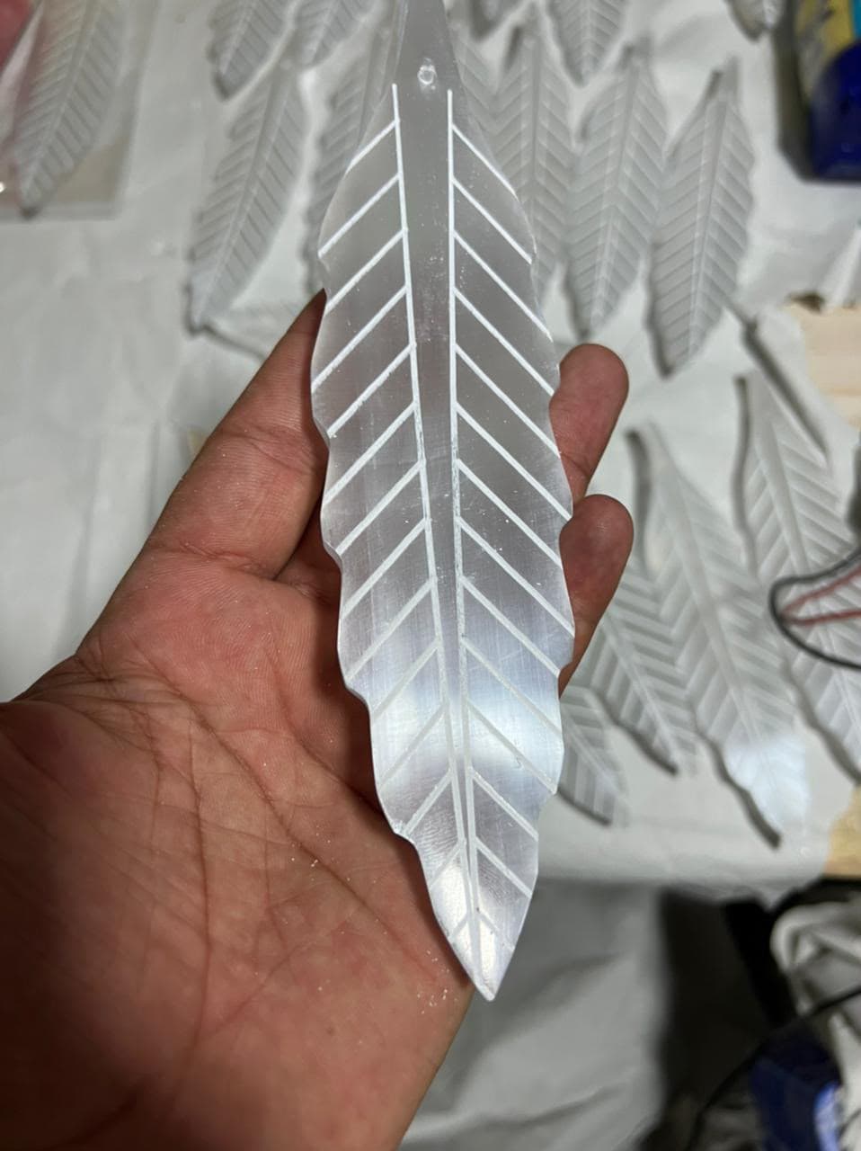 Mano sosteniendo un cristal de selenita blanca translúcida con una talla detallada en forma de pluma.