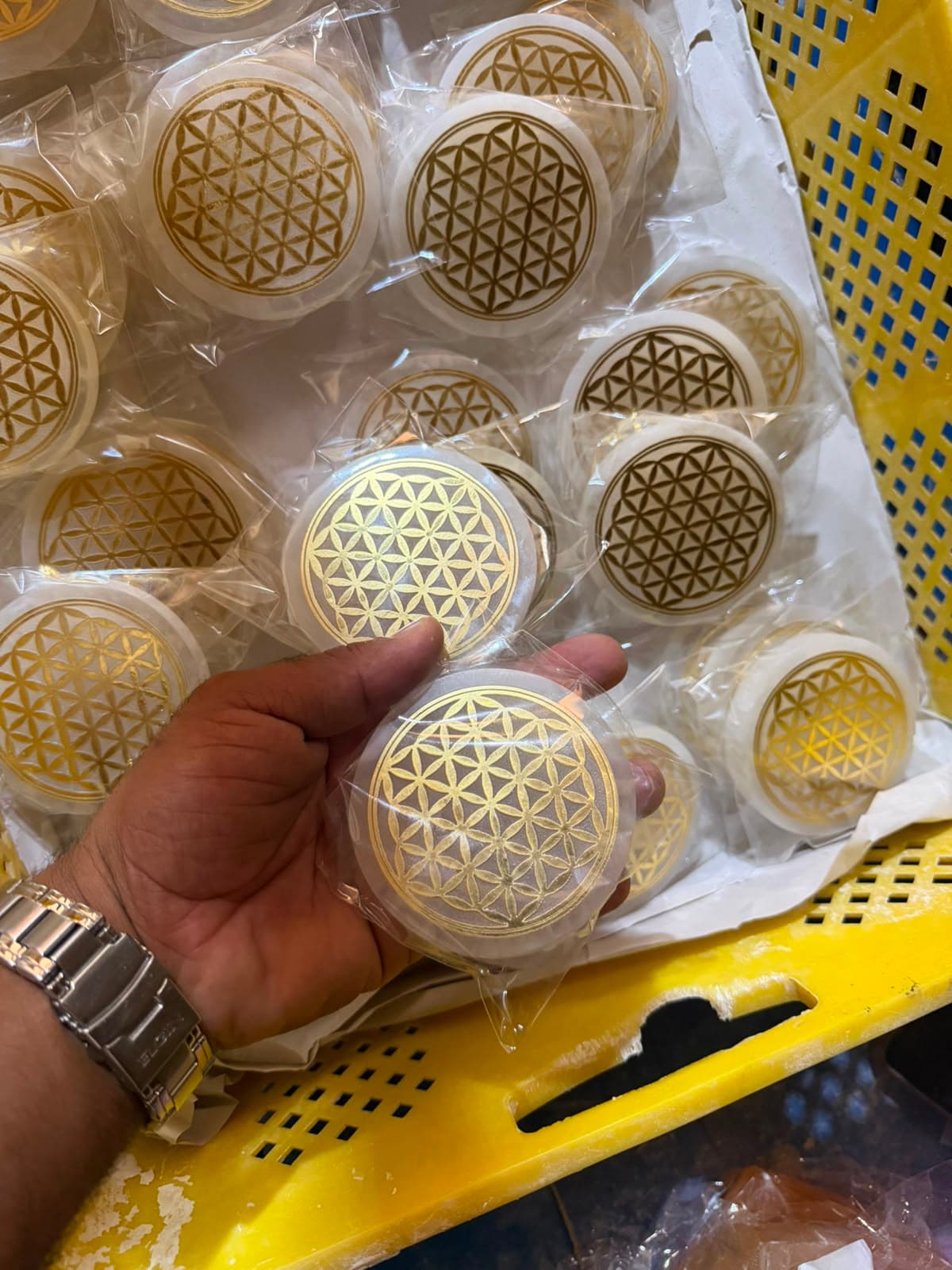 Mano sosteniendo un disco de selenita blanca con el patrón de la Flor de la Vida grabado en oro.