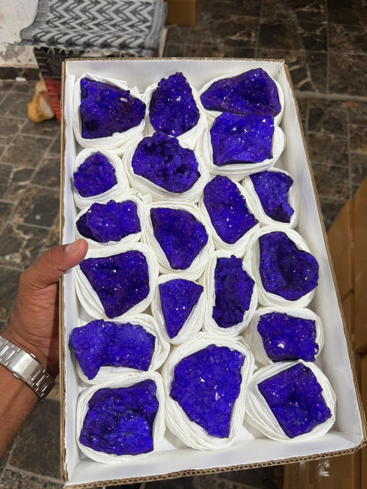 Geodas de cristales de color púrpura intenso envueltas individualmente en papel blanco dentro de una caja de cartón.
