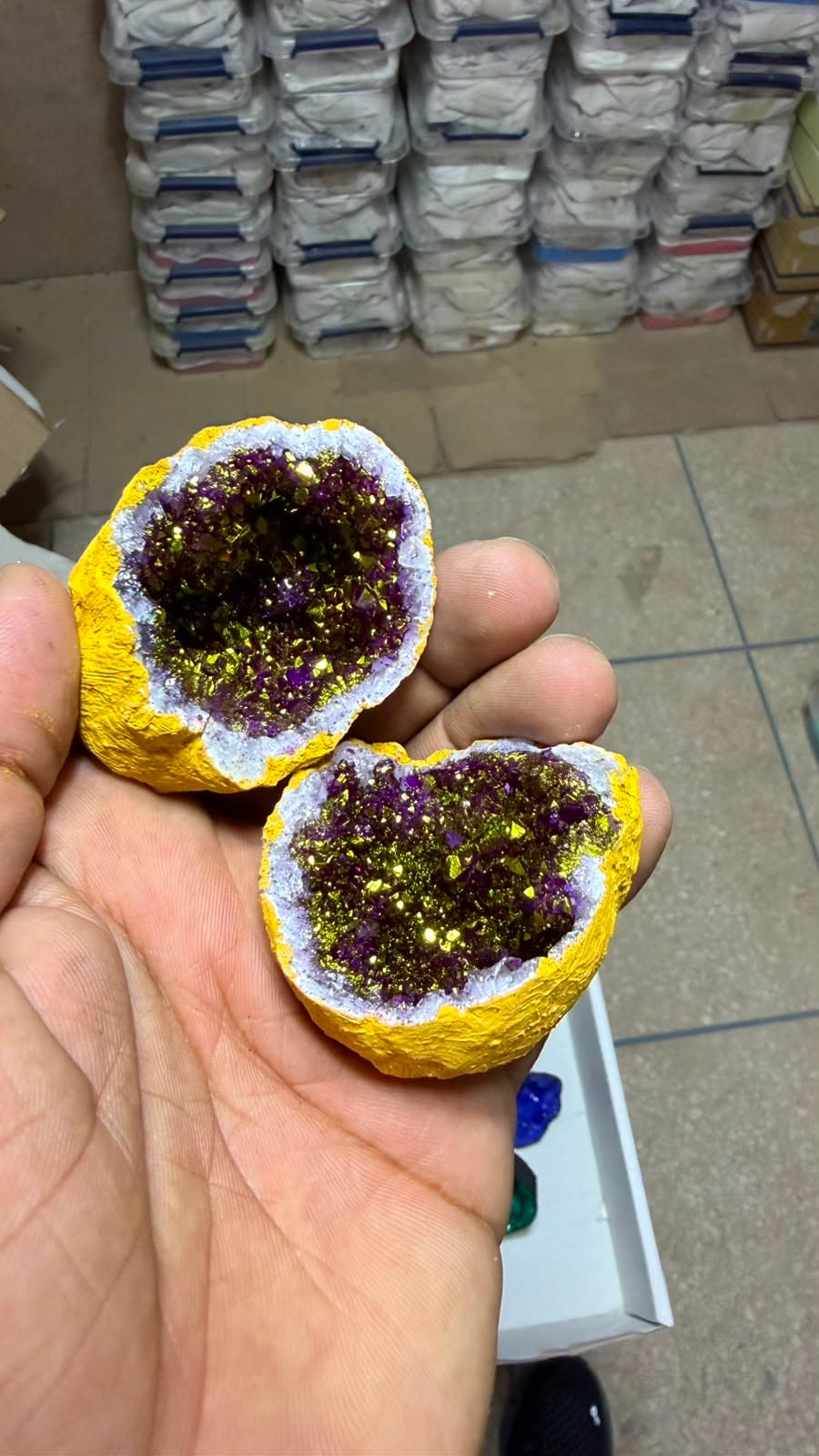 Mano sosteniendo las dos mitades de una geoda amarilla que contiene cristales brillantes en tonos púrpura y dorado.